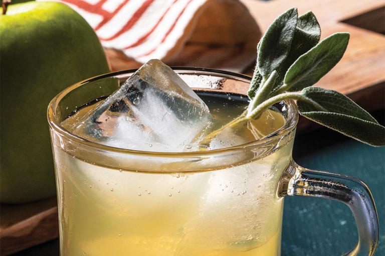 a glass of bubbly cider garnished with sage