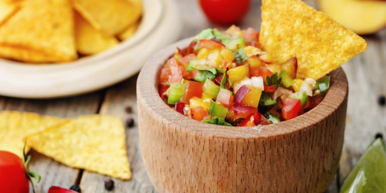 A tortilla chip dipped into fresh peach salsa